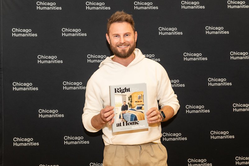 alt text: a man in a white hoodie holding a book infront of a black background