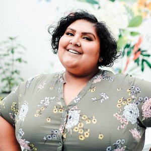 portrait of Sonalee, with a bright smile, floral print dress, and her hands on her hips looking happy and smiling slightly