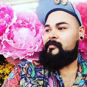 portrait of man with fluffy beard and nose ring against bright pink flowers